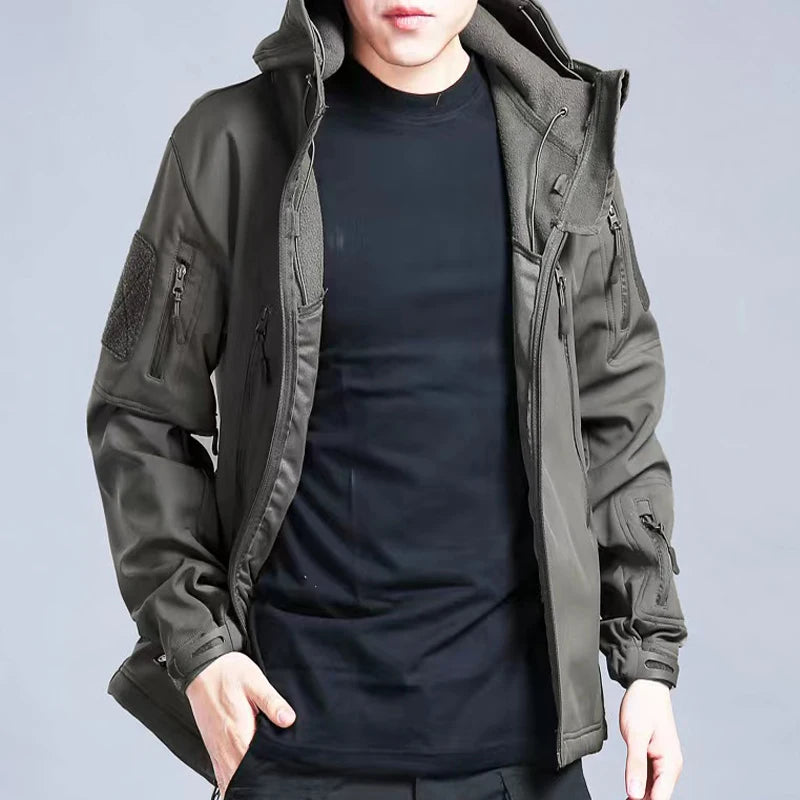 Person wearing a dark green tactical jacket on a gray background