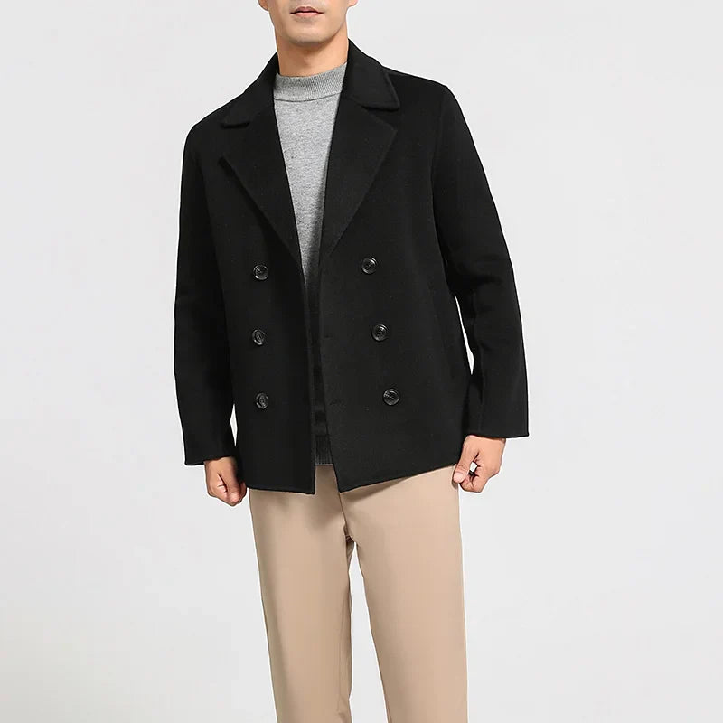 Person wearing a black coat with a gray shirt and beige pants on a white background