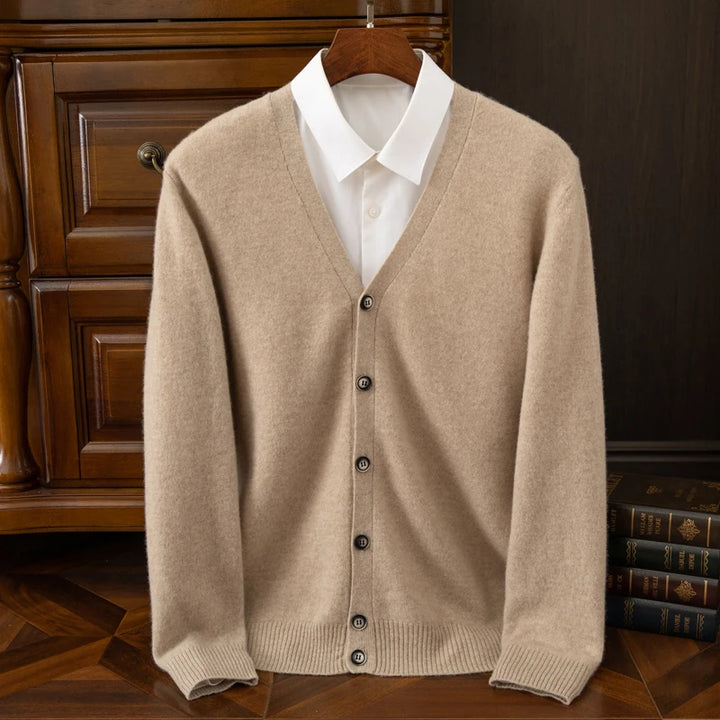 Beige cardigan over a white shirt on a wooden hanger against a dark background.