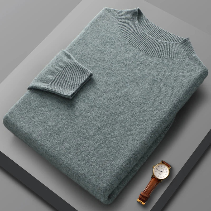 Folded teal sweater on a gray surface with a watch beside it