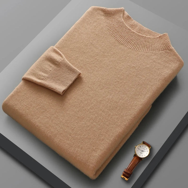 Folded beige sweater on a gray surface with a watch beside it