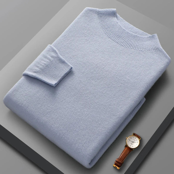 Folded light blue sweater on a gray surface with a watch beside it