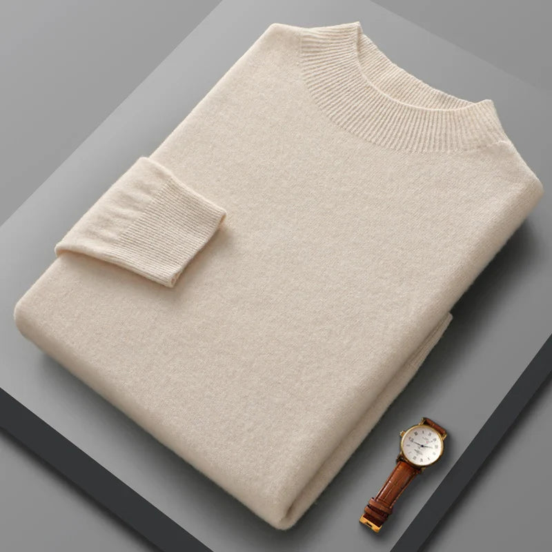 Folded beige sweater on a gray surface with a watch beside it