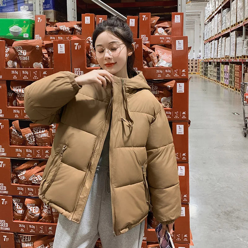 Person wearing a brown puffer jacket in a warehouse setting with stacked boxes.