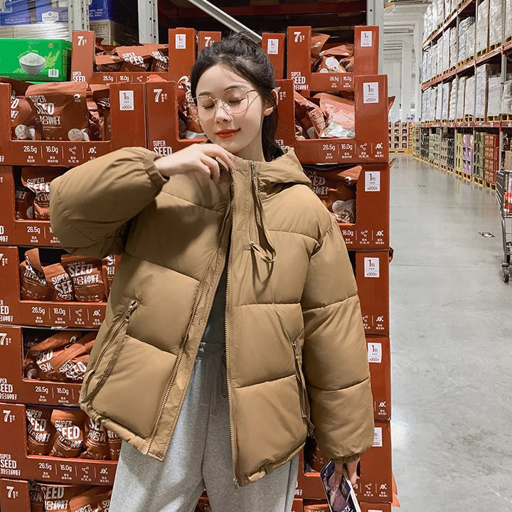 Person wearing a brown puffer jacket in a warehouse setting with stacked boxes.