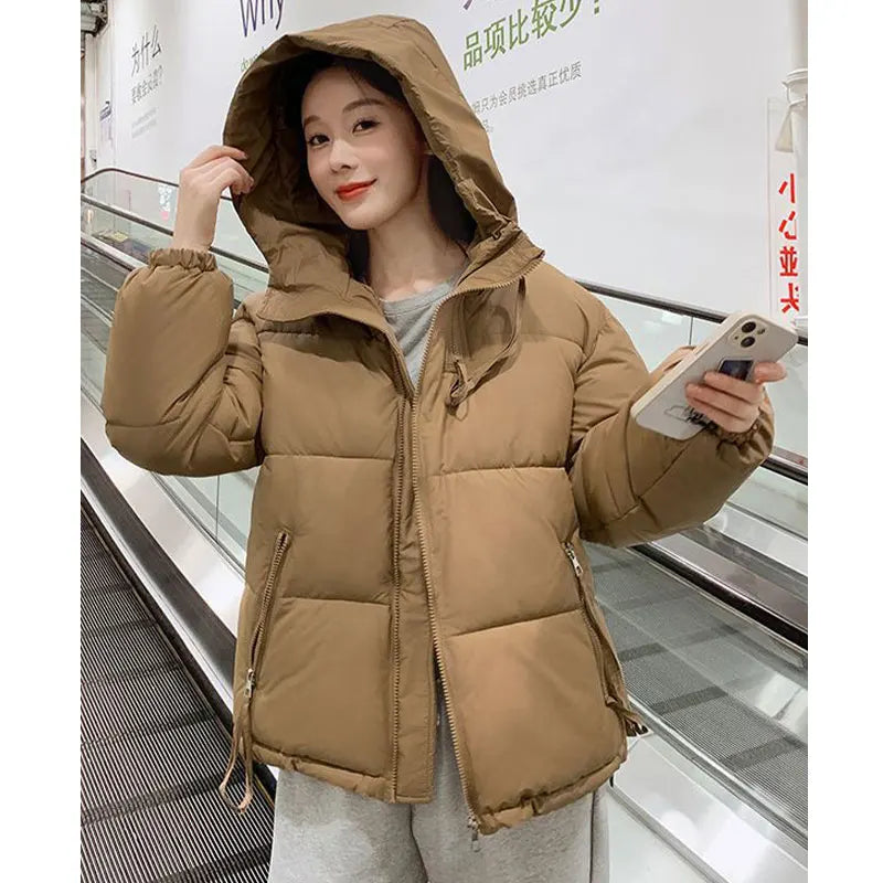 Person wearing a brown puffer jacket holding a phone in an indoor setting.