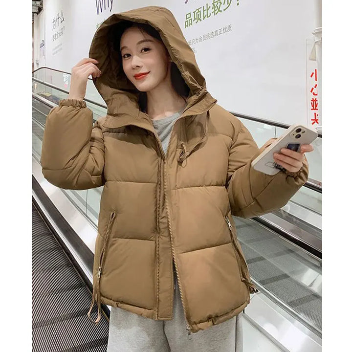 Person wearing a brown puffer jacket holding a phone in an indoor setting.