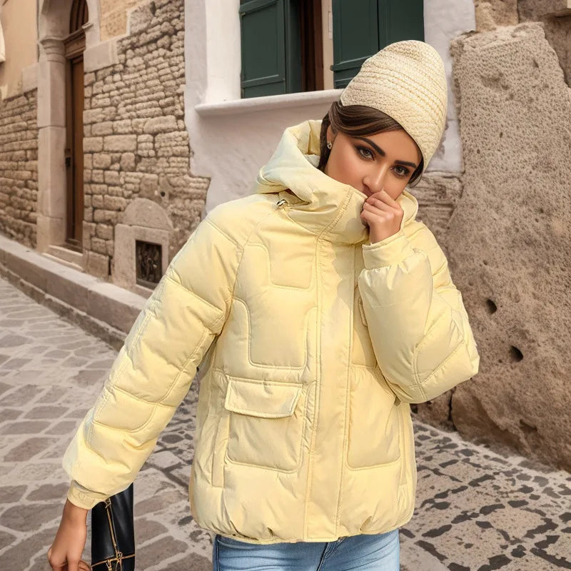 Woman wearing a light yellow puffer jacket and beige beanie standing on a stone-paved street.