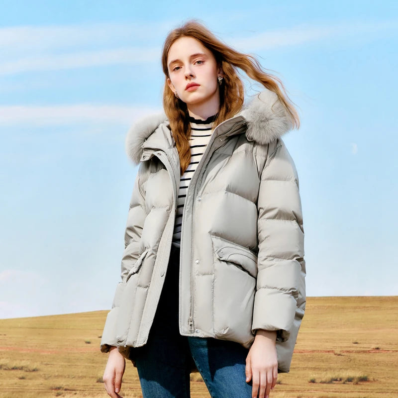 Person wearing a light gray puffer jacket with fur hood in an open field.