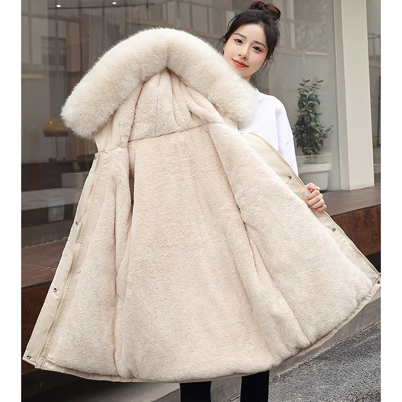 Woman wearing a beige winter coat with a large fur hood indoors.