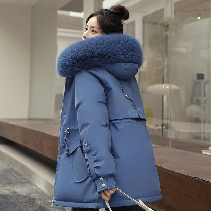 Woman wearing a blue winter coat with a fur-lined hood in an indoor setting.
