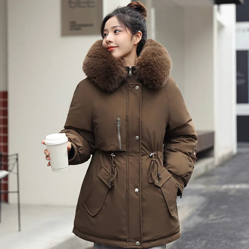 Woman wearing a brown parka with a fur-lined hood, holding a coffee cup.