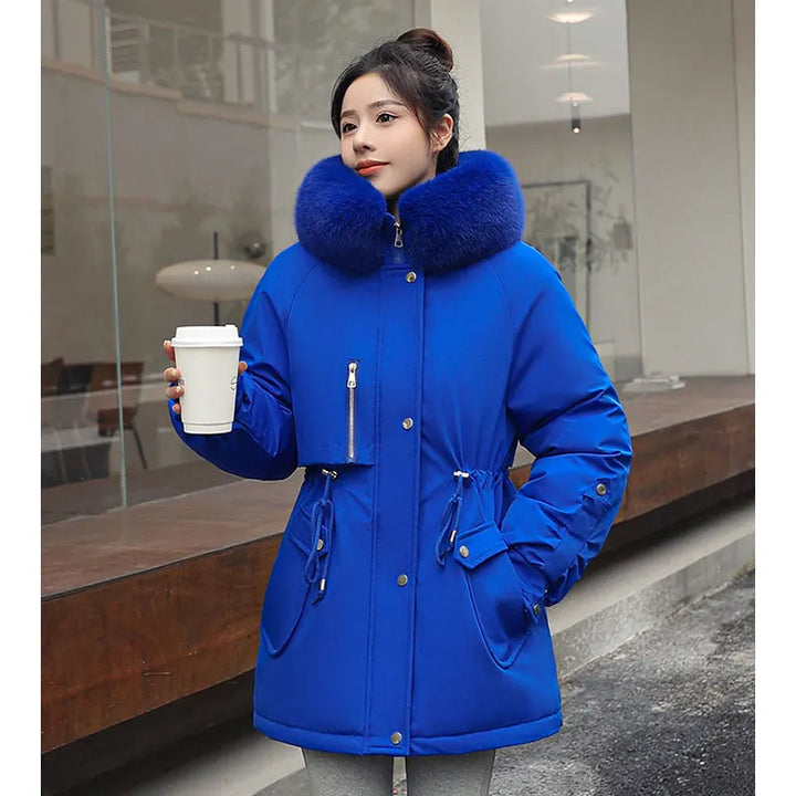 Woman wearing a blue coat with a fur-lined hood, holding a white cup.