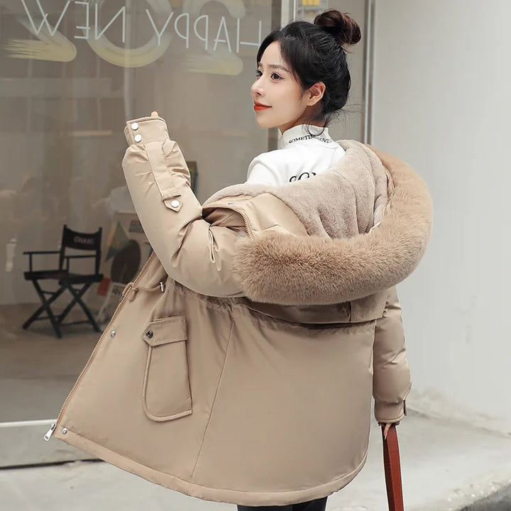 Woman wearing a beige winter coat with fur trim in an indoor setting.