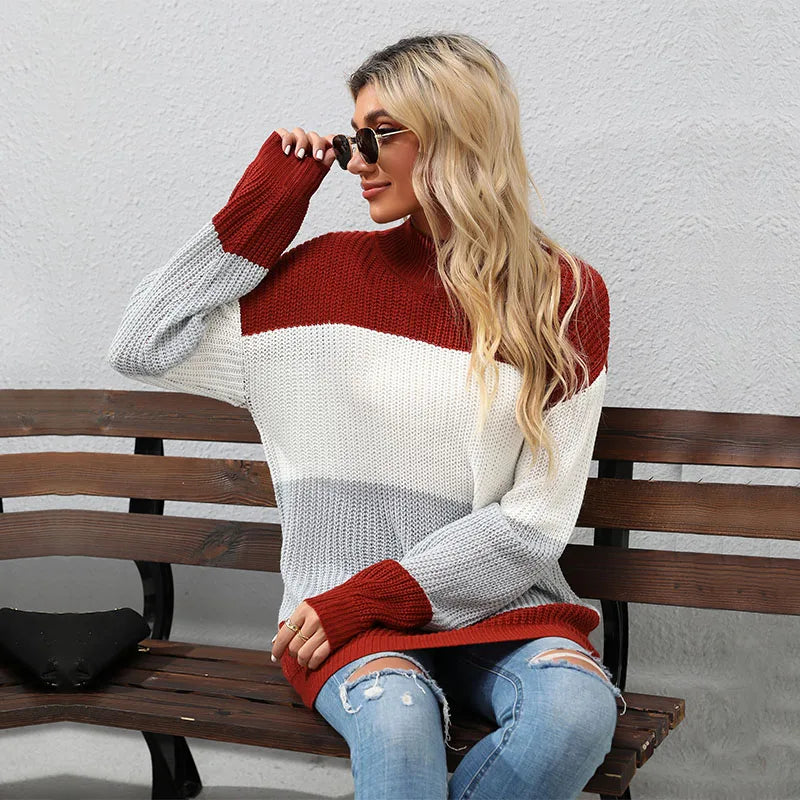 Woman wearing a colorful sweater sitting on a bench against a plain wall.