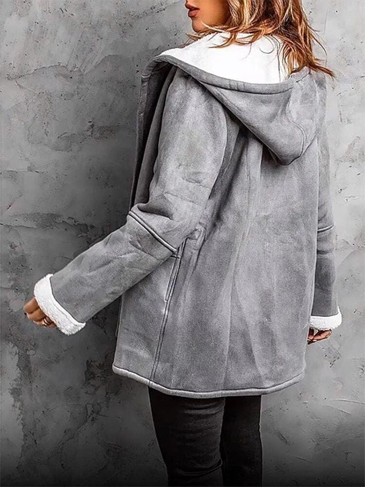 Person wearing a gray hooded coat with white trim against a gray concrete wall.