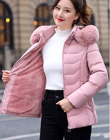 Woman wearing a pink puffer jacket with a fur-lined hood on a city street.