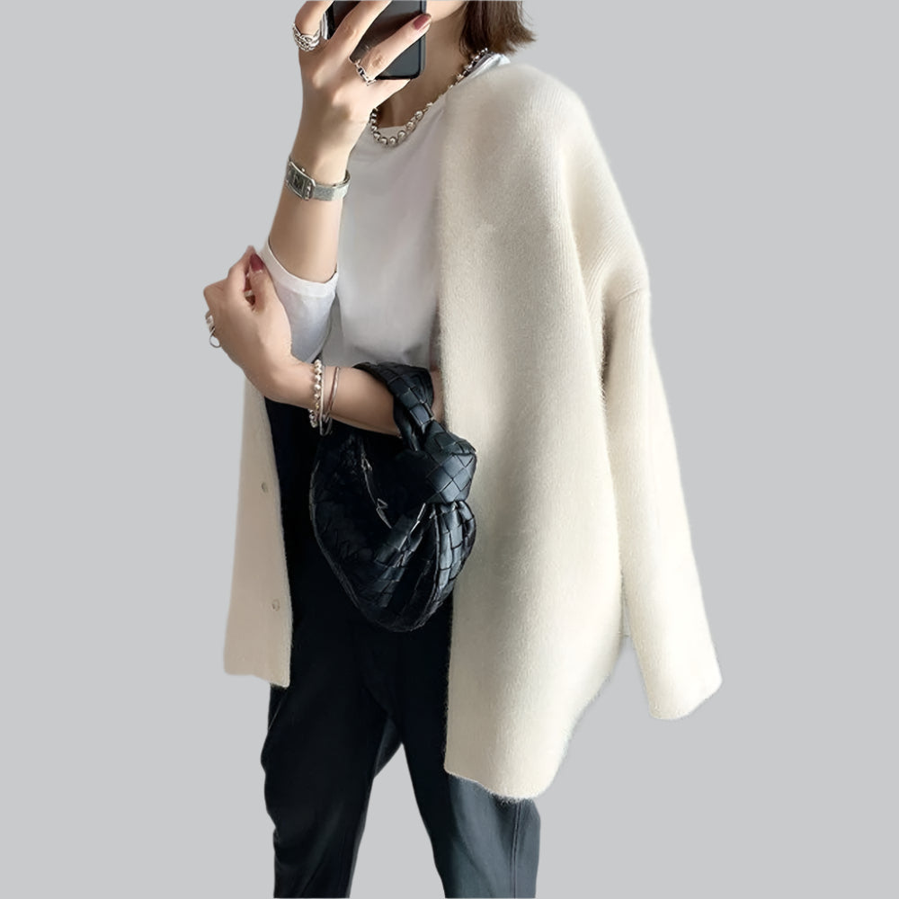 Person wearing a white sweater over a black top with a black handbag on a light gray background