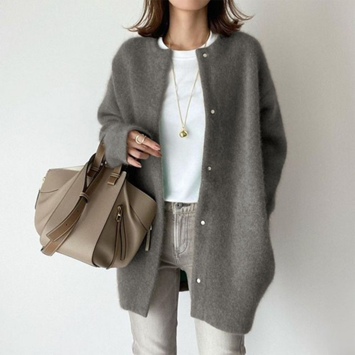 Person wearing a gray cardigan, white shirt, and jeans, holding a beige handbag on a plain background