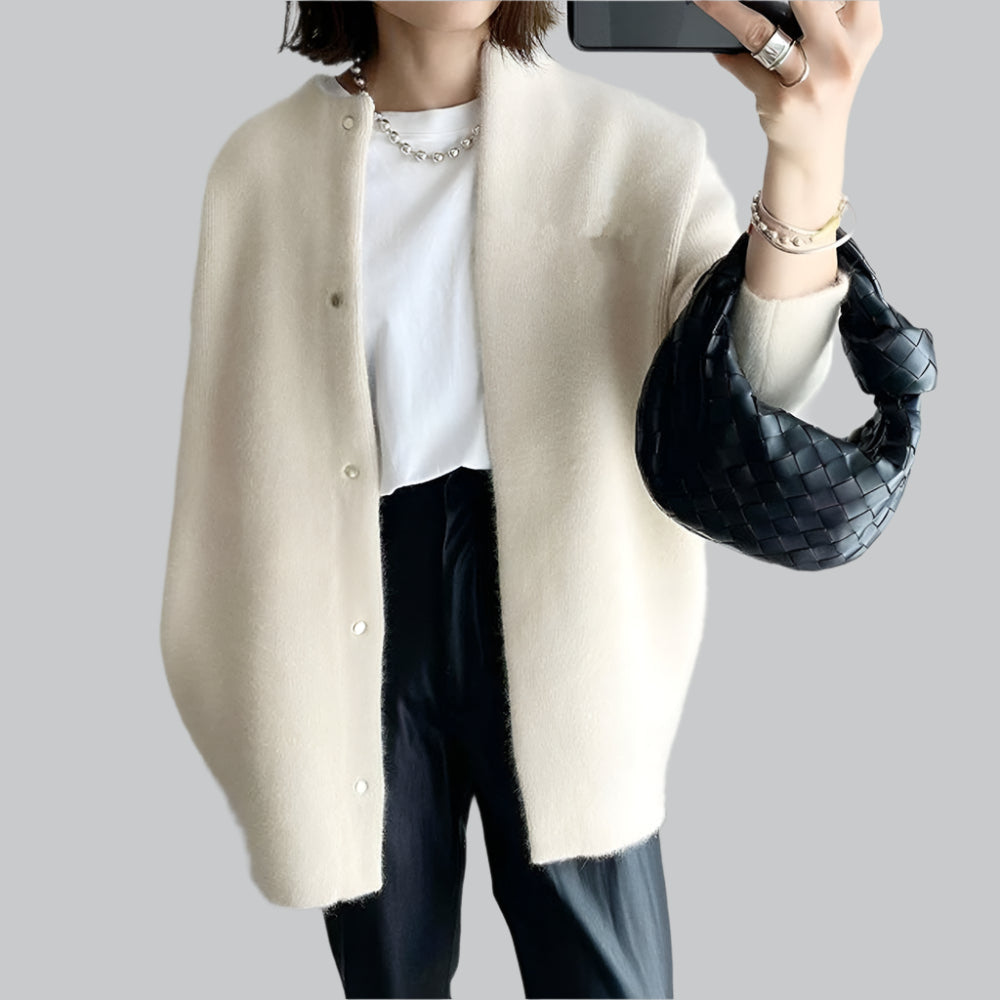 Person wearing a beige cardigan over a white shirt with black pants, holding a black handbag.