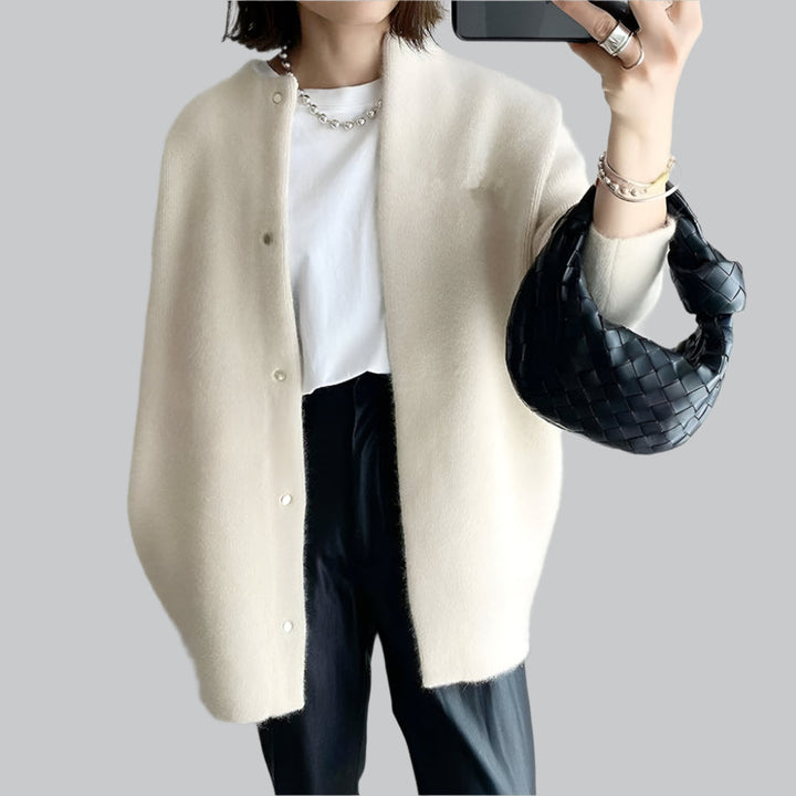 Person wearing a beige cardigan over a white shirt with black pants, holding a black handbag.