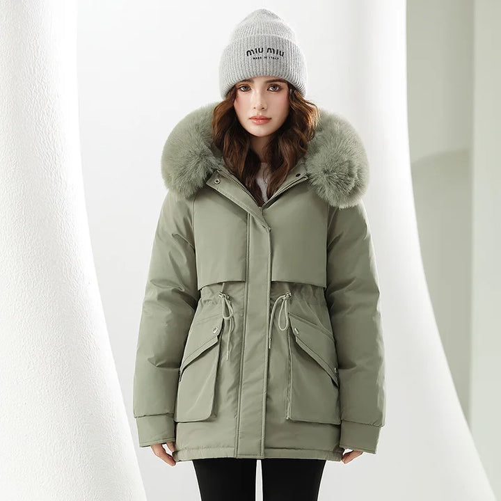 Woman wearing a green parka with fur hood and a gray beanie on a white background