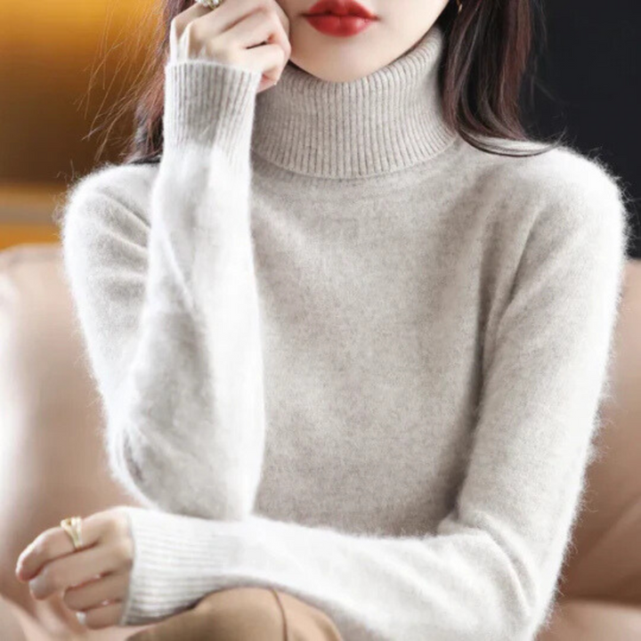 Person wearing a light gray turtleneck sweater with a blurred background