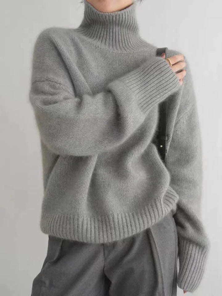 Person wearing a gray turtleneck sweater against a plain background