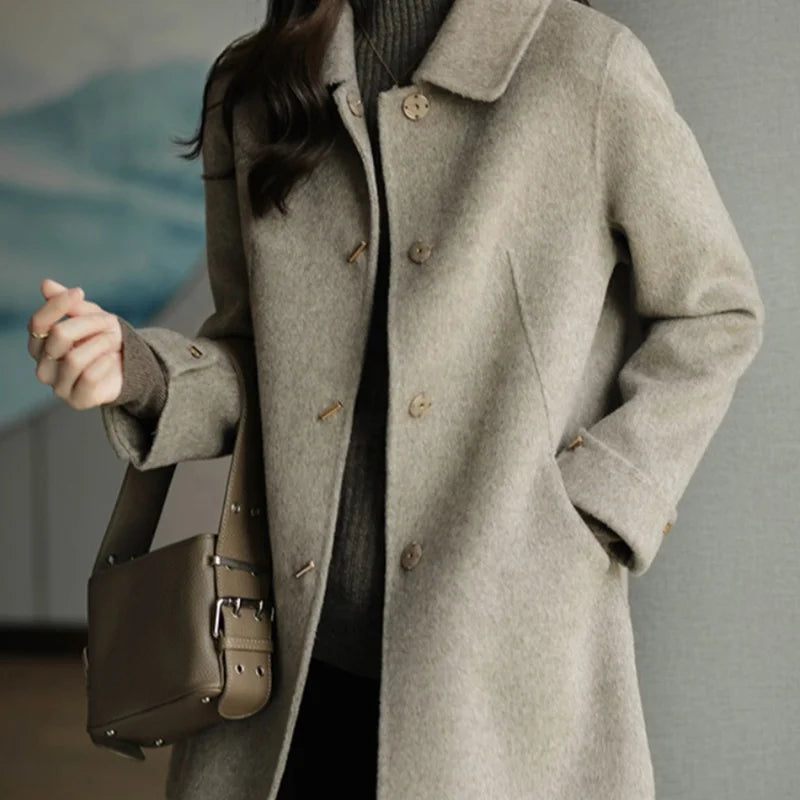 Person wearing a gray coat holding a brown bag against a neutral background