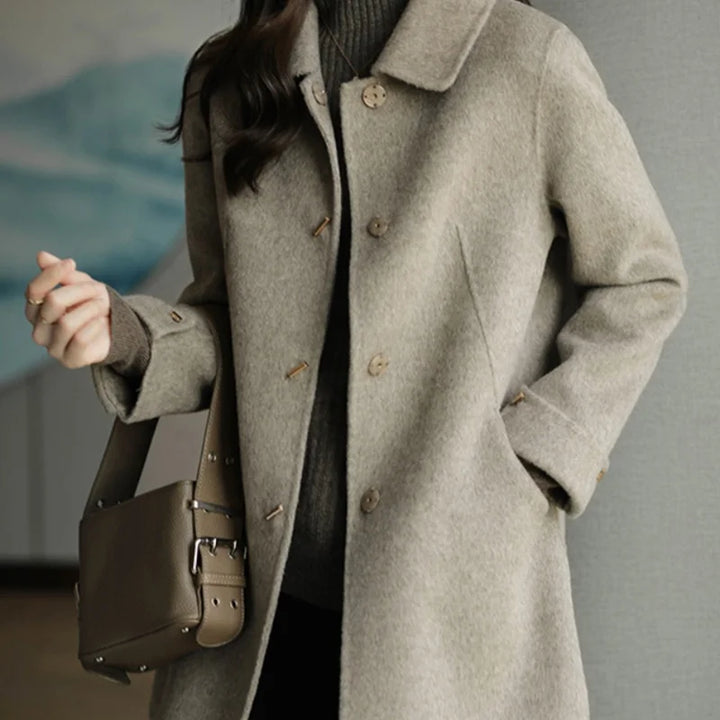 Person wearing a gray coat holding a brown bag against a neutral background