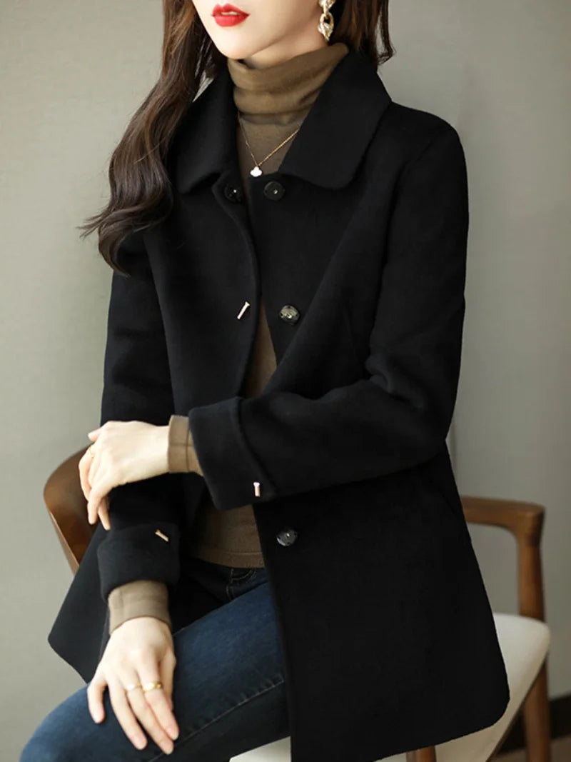 Woman wearing a black coat sitting on a chair with a neutral background