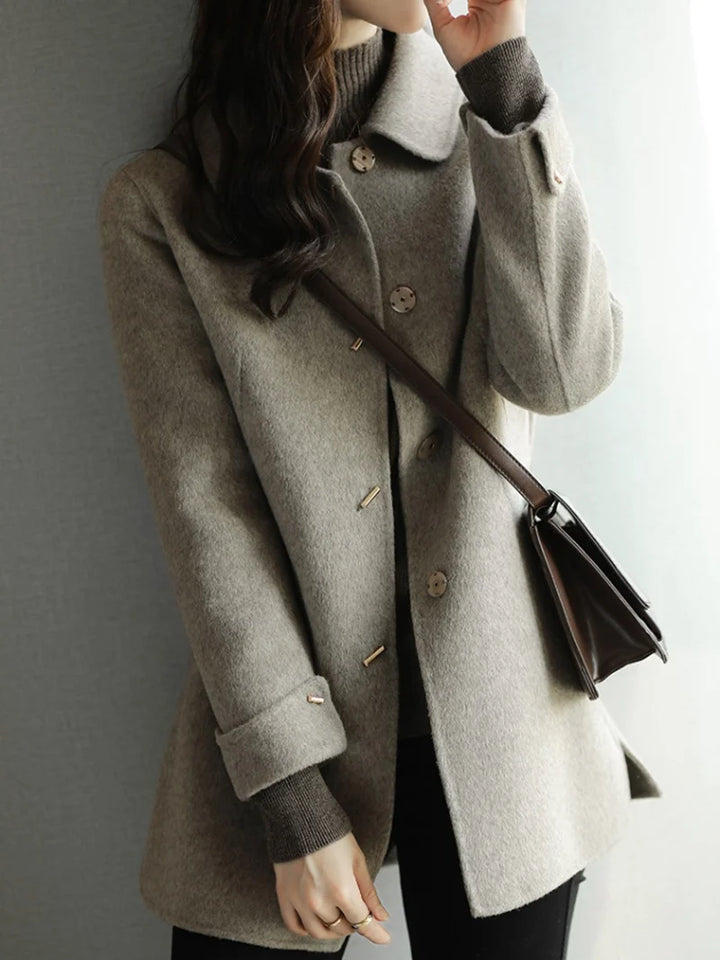 Person wearing a gray coat with a brown handbag against a neutral background