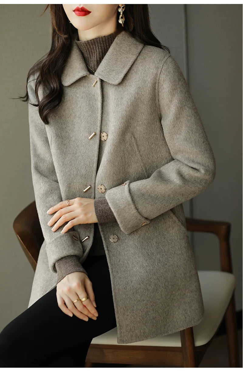 Woman wearing a gray coat sitting on a chair with a neutral background