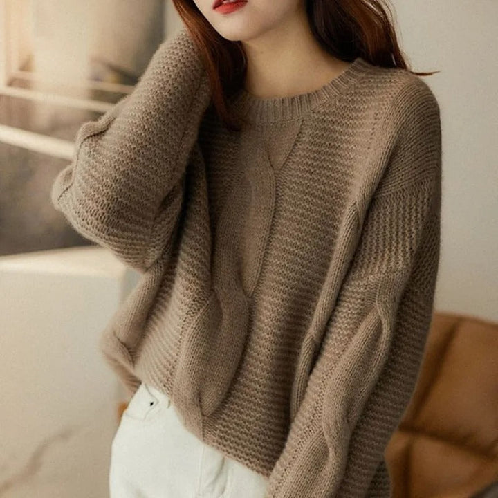Person wearing a brown knitted sweater in a blurred indoor setting