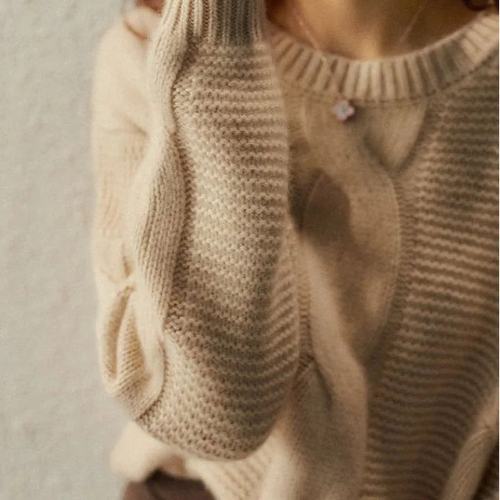 Close-up of a beige knitted sweater with cable knit pattern on a neutral background